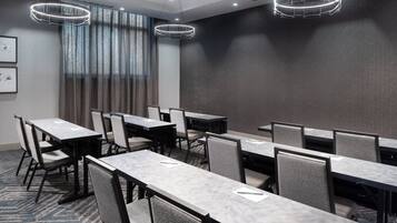 A conference room with multiple tables and chairs, large windows with curtains, and modern lighting fixtures.
