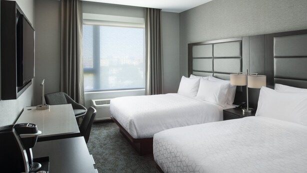 A hotel room with two beds, a desk, a chair, a TV, and a large window with curtains. - Holiday Inn Express Boston Logan Airport - Revere by IHG (Revere)