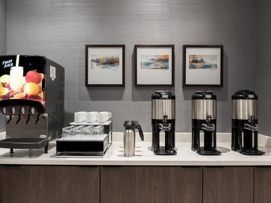 A coffee station with multiple coffee makers and a fruit juice dispenser, glasses, and cups.