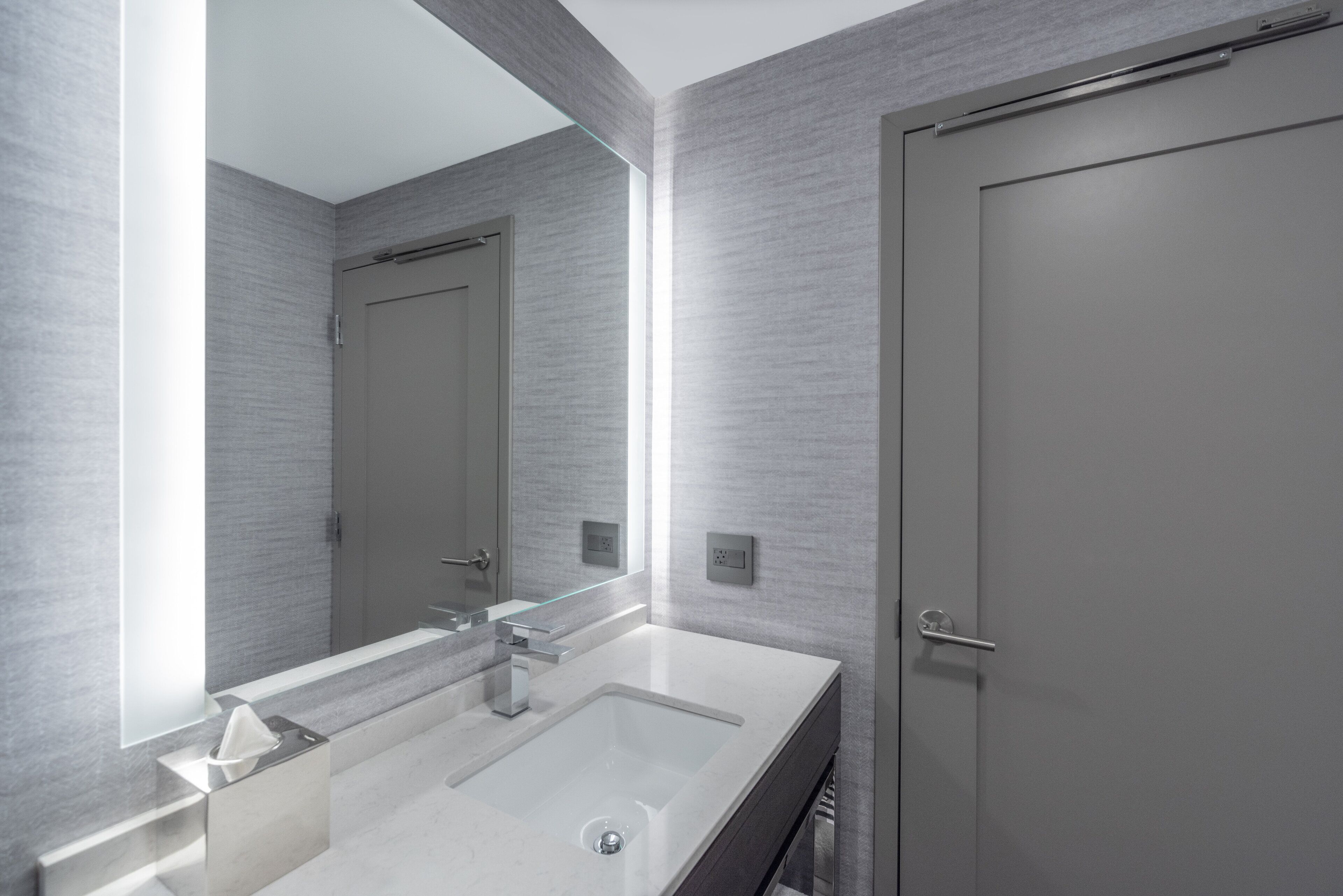 A modern bathroom with a large mirror, two sinks, and a door.