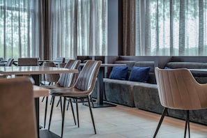 Un comedor moderno con una variedad de opciones de asientos, incluyendo mesas y sofás, y vistas a árboles a través de amplias ventanas.
