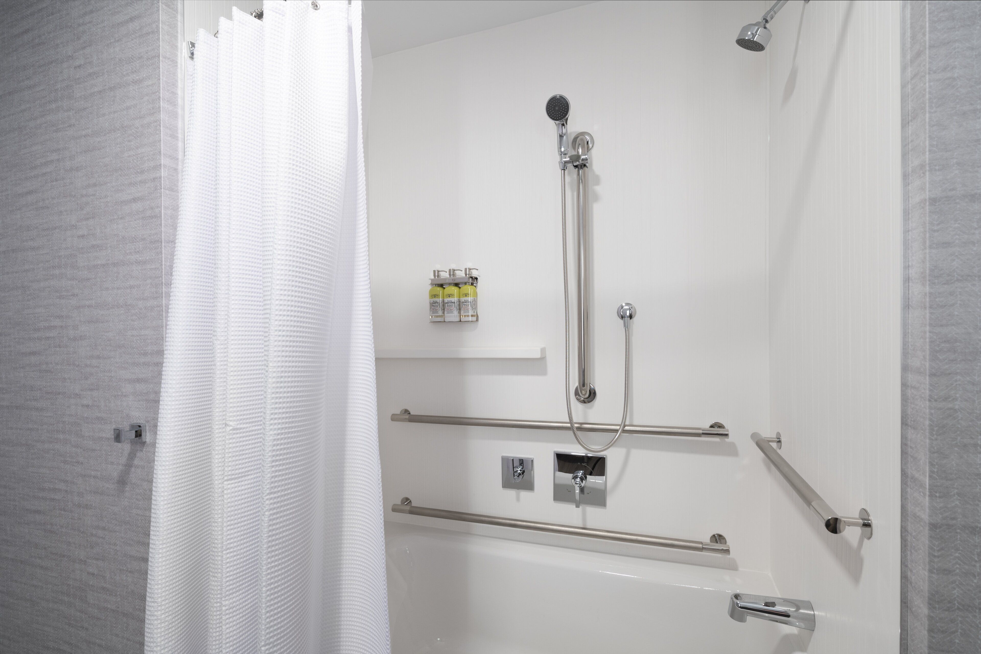 A modern bathroom with a walk-in shower, grab bars, and a mounted soap dispenser.