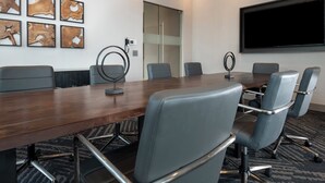 A conference room with a long table, six chairs, a projector screen, and abstract wall art. - Holiday Inn Express Boston Logan Airport - Revere by IHG (Revere)