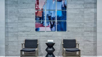 Two wooden chairs with woven seats and backs, a black sculptural object, and a large abstract painting on a grey wooden wall.