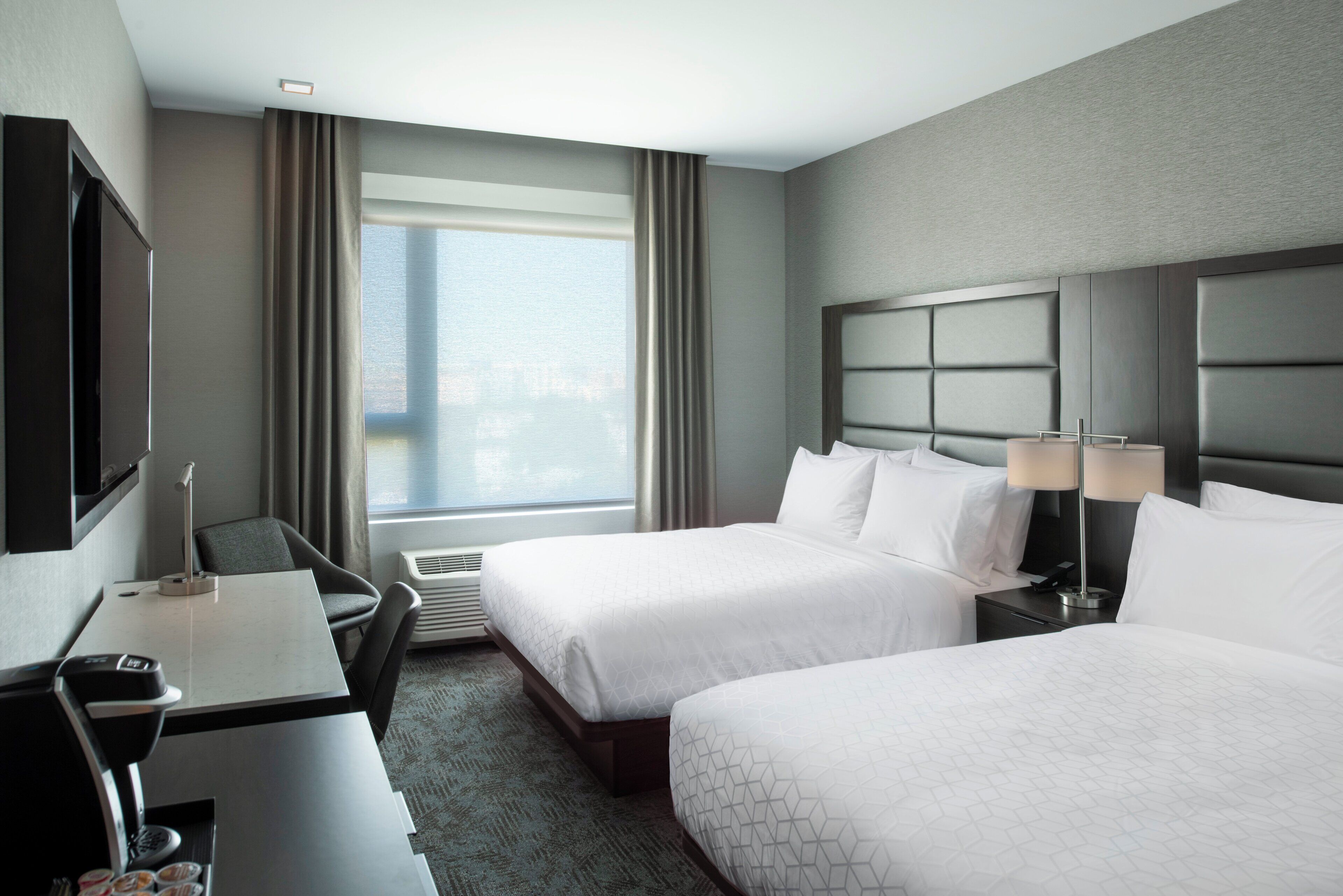 A hotel room with two beds, a desk, a chair, a TV, and a window with curtains.