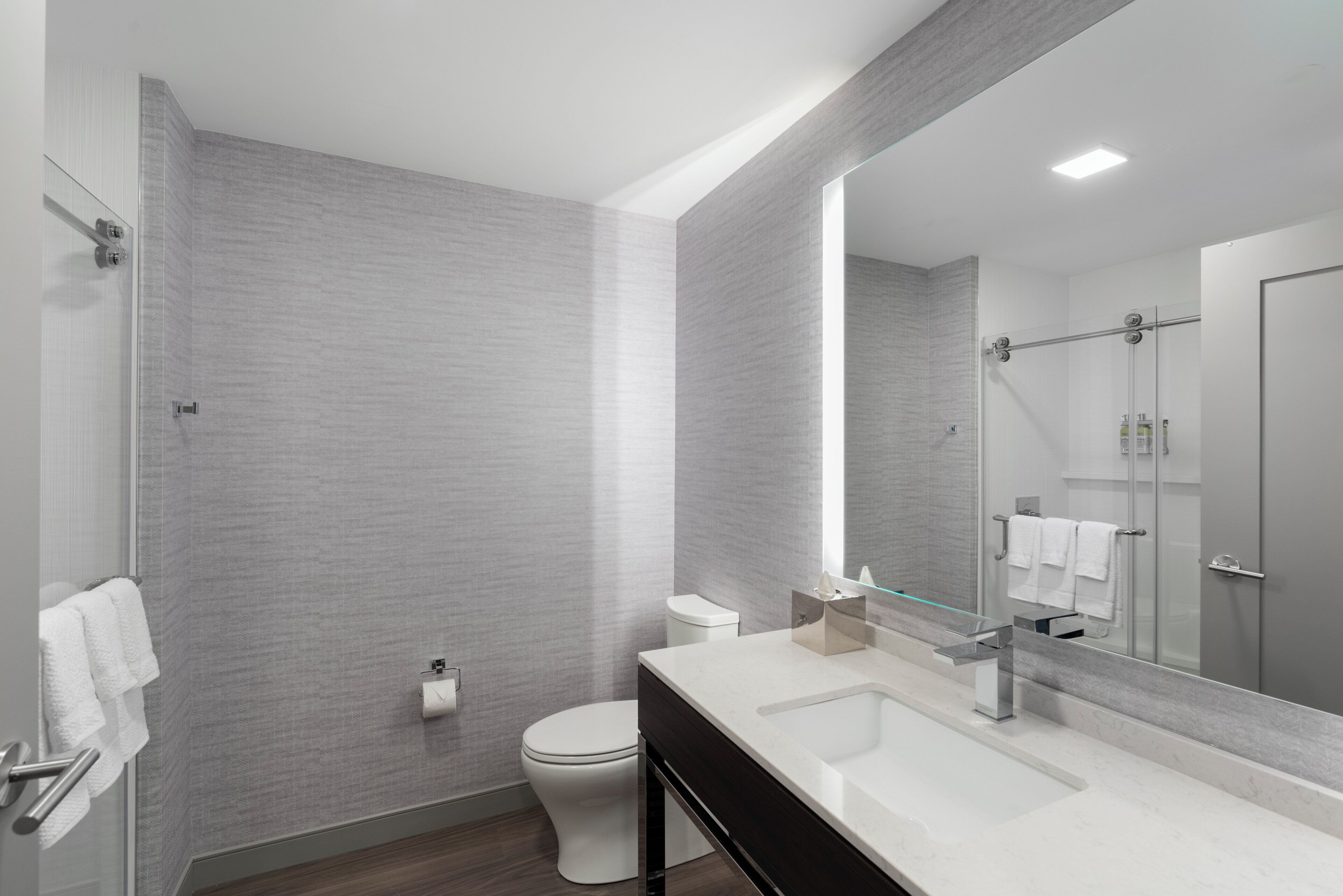 Un baño moderno con un espejo grande, un lavamanos blanco y un inodoro.