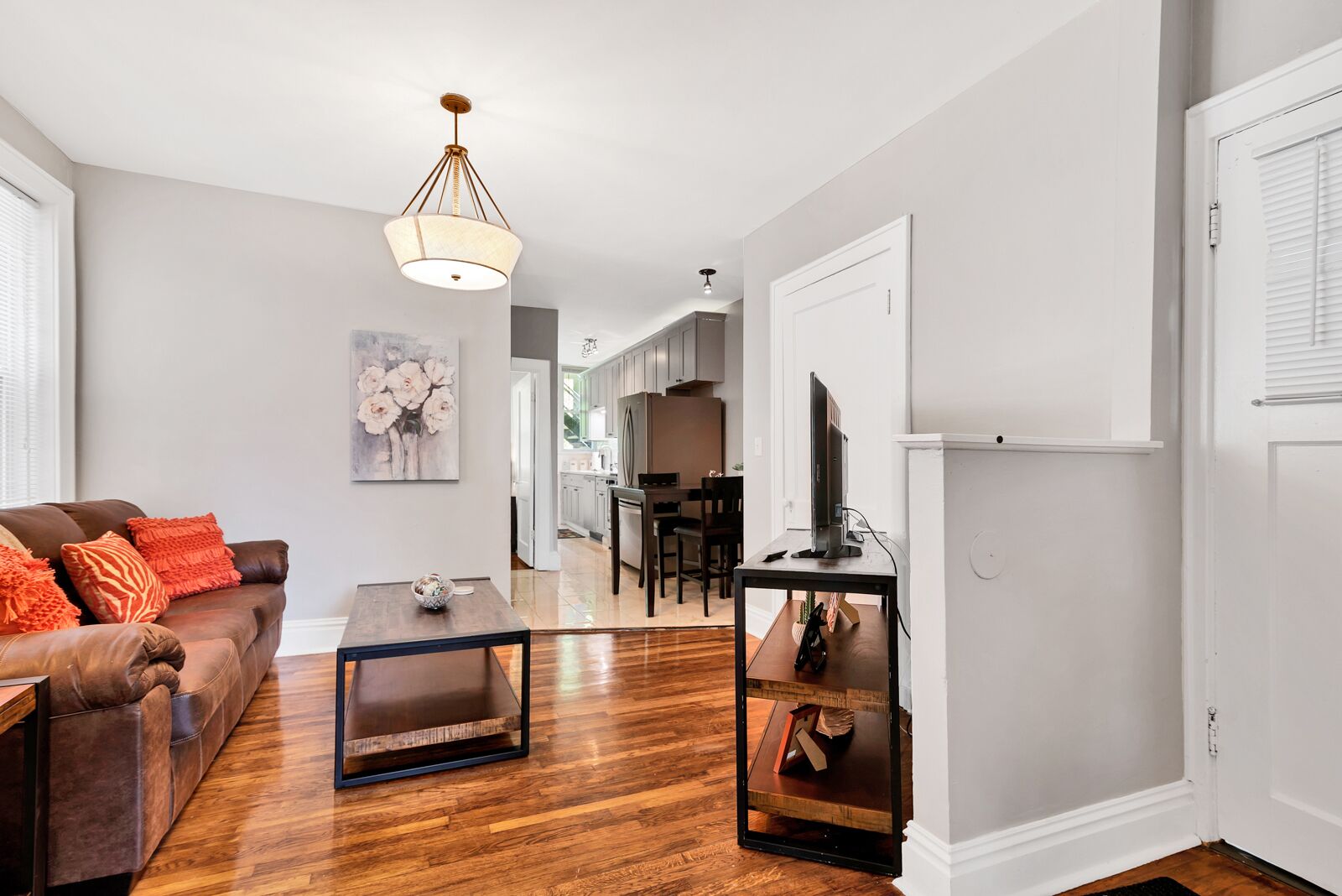 A modern living room with hardwood flooring, a brown leather sofa, a coffee table, and a television on a stand.