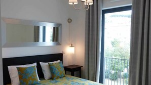 A hotel room with a bed, a nightstand, a wall-mounted lamp, and a view of the outdoors through a balcony. - Central. High speed WIFI & FREE Parking (Lisboa)