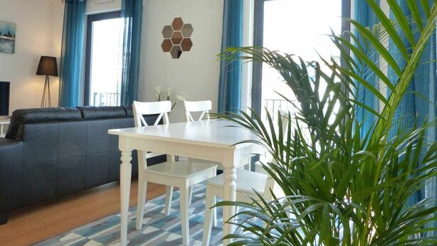 A living room with a sofa, a dining table with chairs, a chandelier, and a large window with blue curtains. - Central. High speed WIFI & FREE Parking (Lisboa)