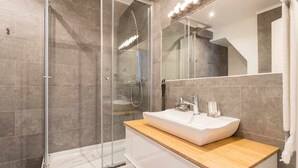 Un baño moderno con ducha de vidrio, lavamanos blanco y encimera de madera.