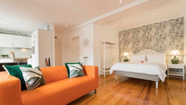 Un dormitorio moderno con una cama blanca, una mesita de noche con lámpara y suelo de madera.