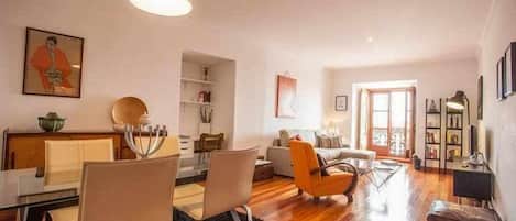 Una sala de estar moderna con comedor, piso de madera y un ventanal que deja entrar abundante luz natural.