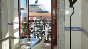 En balkon med en plantekasse, udsigt til et krydstogtskib og en sort gulvlampe.