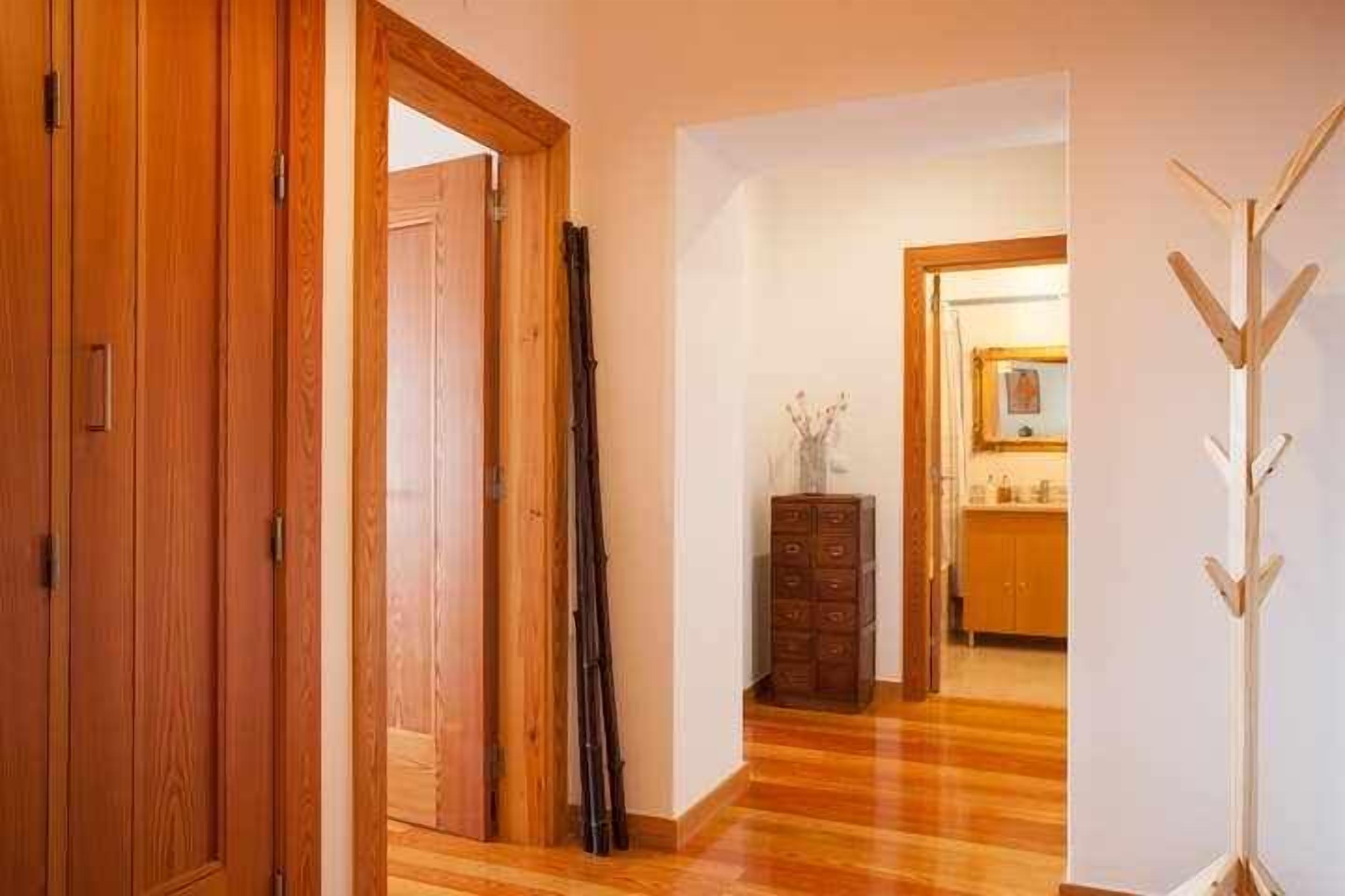A hallway with wooden flooring, a wooden door, a mirror, and a coat rack.