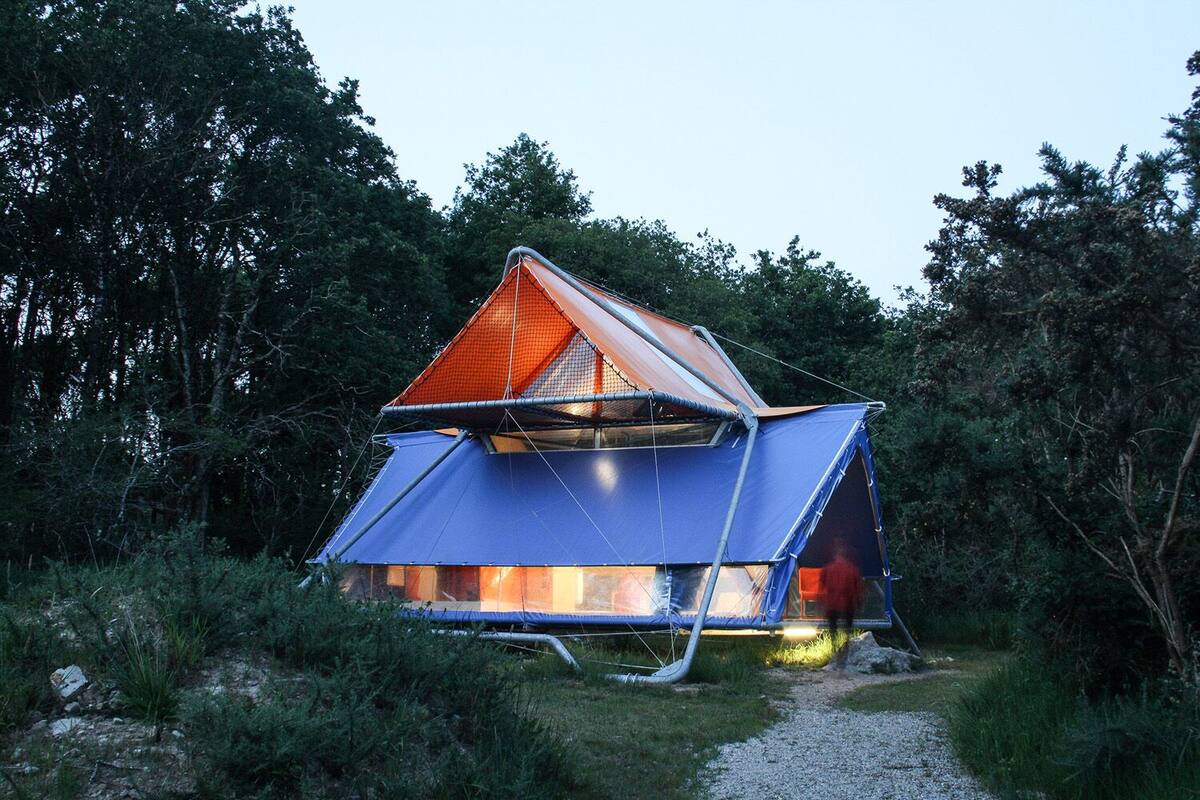 A geodesic dome structure with a triangular roof, surrounded by dense forest.