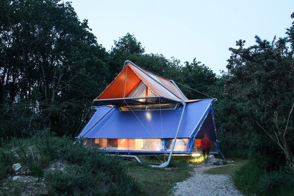 A geodesic dome structure with a triangular roof, surrounded by dense forest. - La Belle Folie (Ploemel)