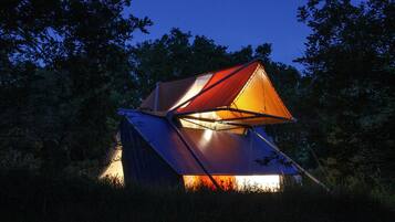Tienda de campaña con techo en forma triangular, rodeada de árboles.