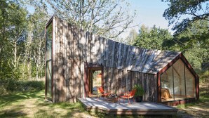 A rustic cabin with a large glass window, a wooden deck, and a cozy seating area. - La Belle Folie (Ploemel)