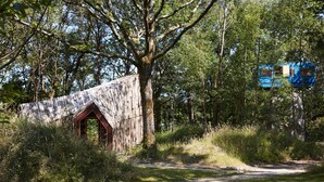 A rustic wooden structure with a red door, surrounded by dense greenery and trees. - La Belle Folie (Ploemel)