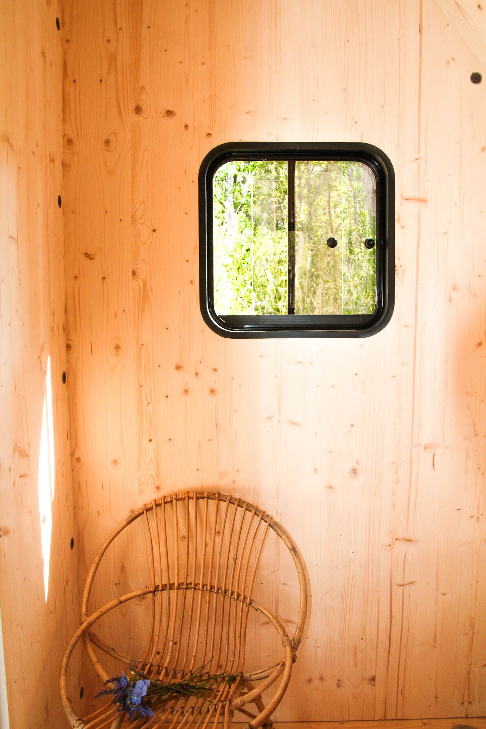 A wooden interior with a window, a wicker chair, and a small table.