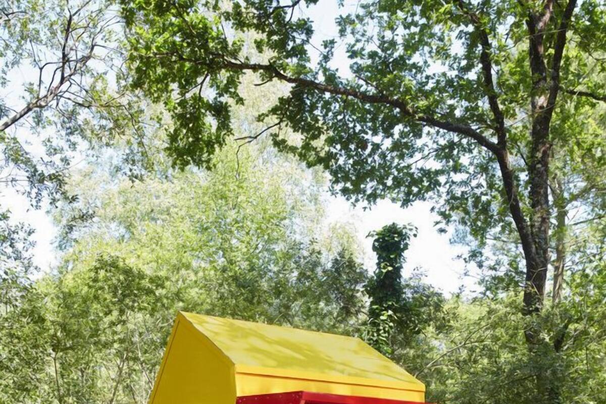 A small yellow cabin with a red awning, a blue suitcase, and a blue chair.