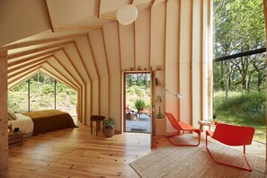 Una habitación acogedora con luz natural, techo inclinado, suelo de madera y un amplio ventanal con vistas al exterior.