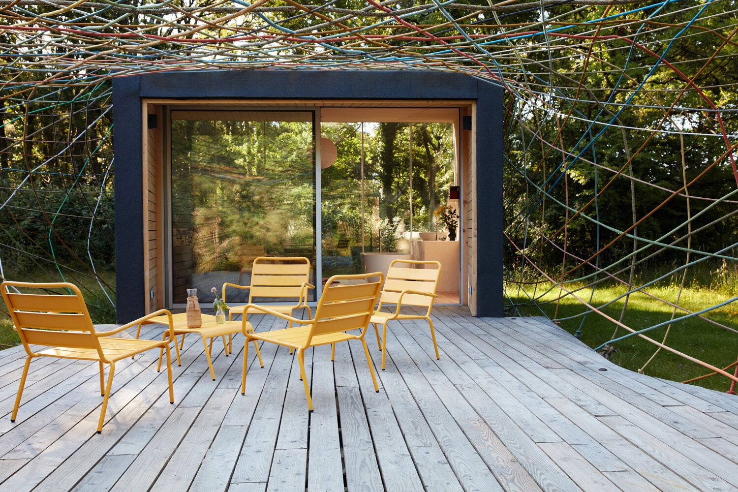 Un espacio moderno para sentarse al aire libre con cerramiento de vidrio, terraza de madera y sillas amarillas.