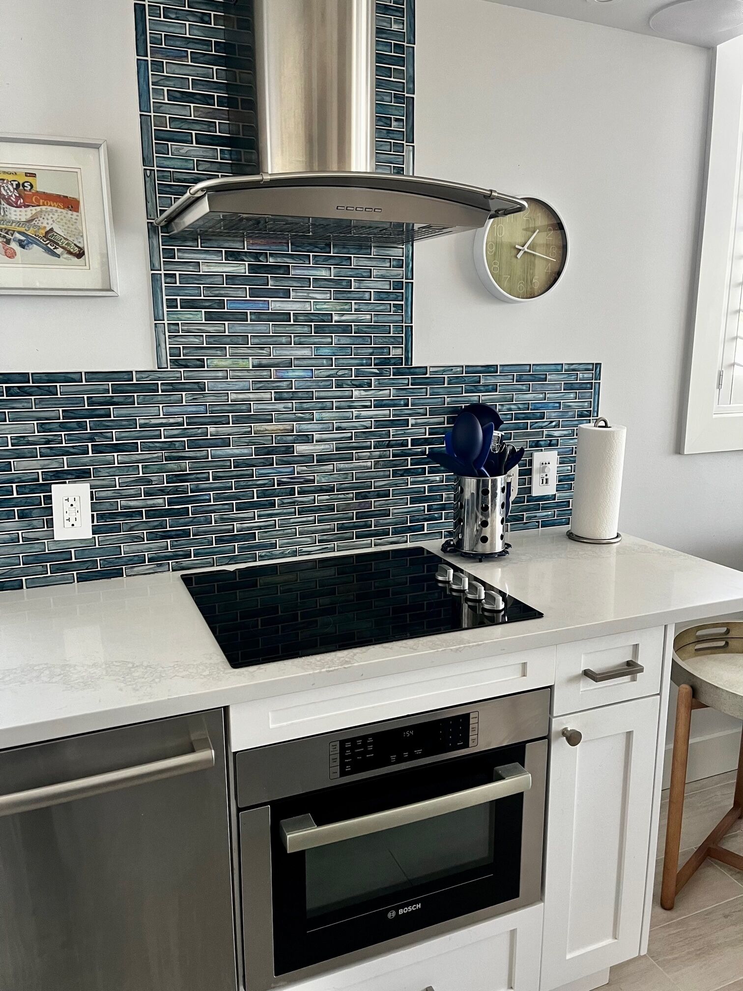 A modern kitchen with a black induction cooktop, stainless steel oven, and a backsplash of blue mosaic tiles.