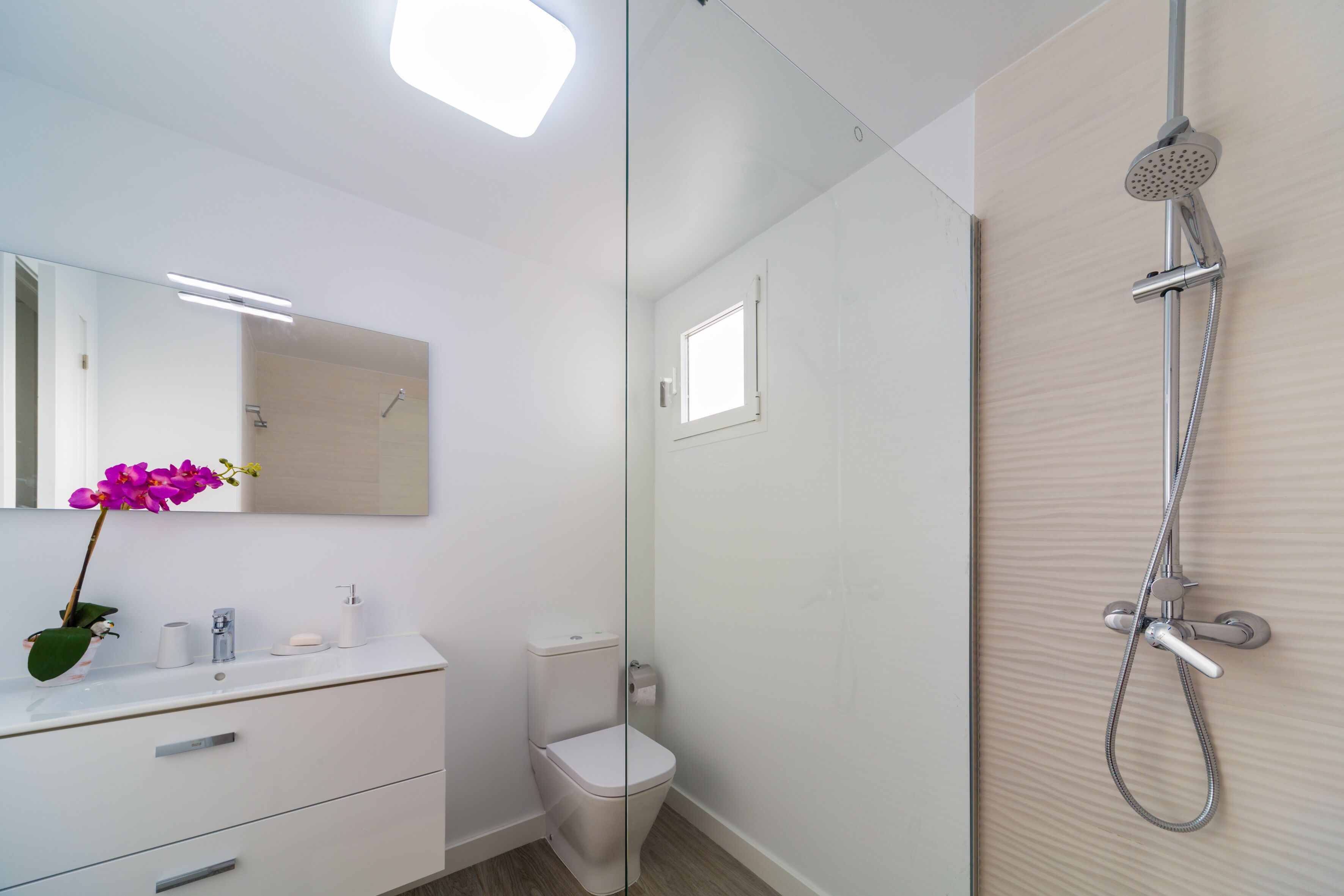 Ein modernes Badezimmer mit Duschkabine aus Glas, einem weißen Waschbecken mit Spiegel und einer Toilette.