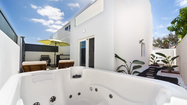 Ein moderner Außenbereich mit Whirlpool, Holztisch und Stühlen, einem gelben Sonnenschirm und einer Treppe, die zu einer Tür führt.