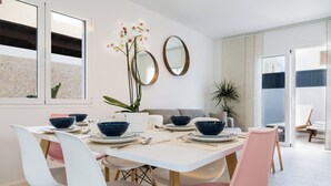 Ein Essbereich mit einem weißen Tisch, pinken und weißen Stühlen sowie blauen Schüsseln. An den Wänden befinden sich zwei Spiegel und in der Ecke eine Pflanze.
