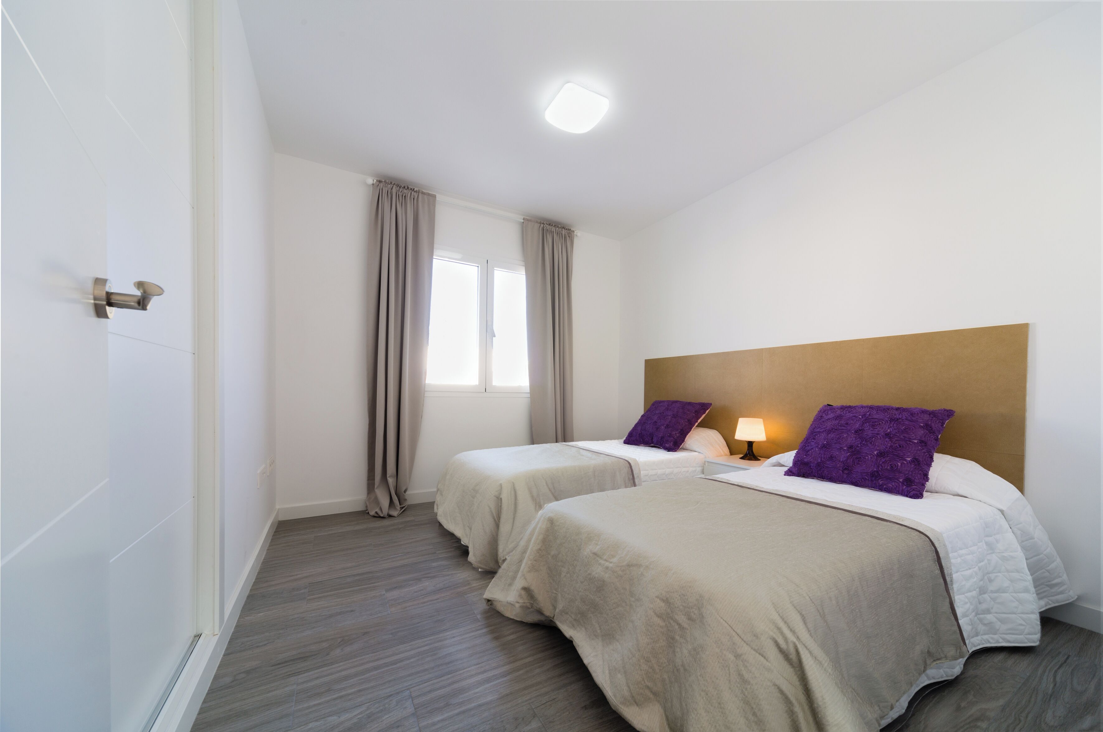 A hotel room with two beds, a wooden headboard, a window with curtains, and a bedside lamp.