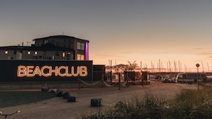 A beach club with a neon sign, a building with multiple windows, and a dock area with boats. - RBR 1021 - Beach Resort Kamperland (Kamperland)