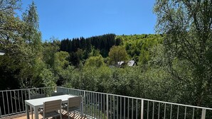 Una terraza de madera con mobiliario exterior, barandilla y vista a un área boscosa.