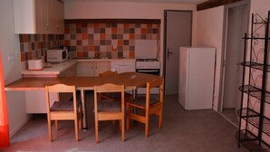 Kompakti keittiö, jossa on puinen pöytä ja tuolit, mikroaaltouuni, liesi ja jääkaappi.