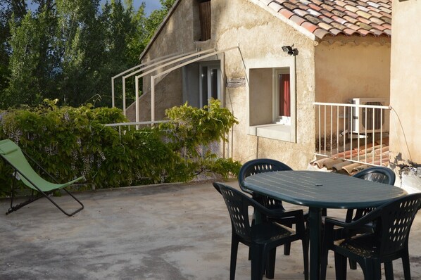 A patio with a table and chairs, a green chair, and a covered area with a window.