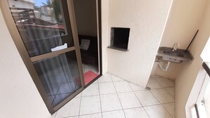 A small, tiled bathroom with a sink, a window, and a door leading to a balcony.