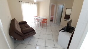 A compact living space with a sofa, a dining table with chairs, a ceiling fan, and a television.