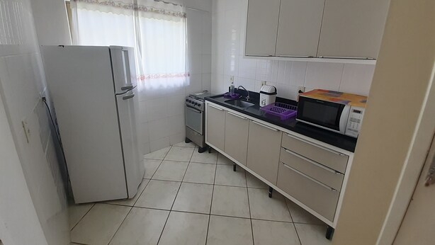 A compact kitchen with white cabinets, a refrigerator, a stove, and a microwave.