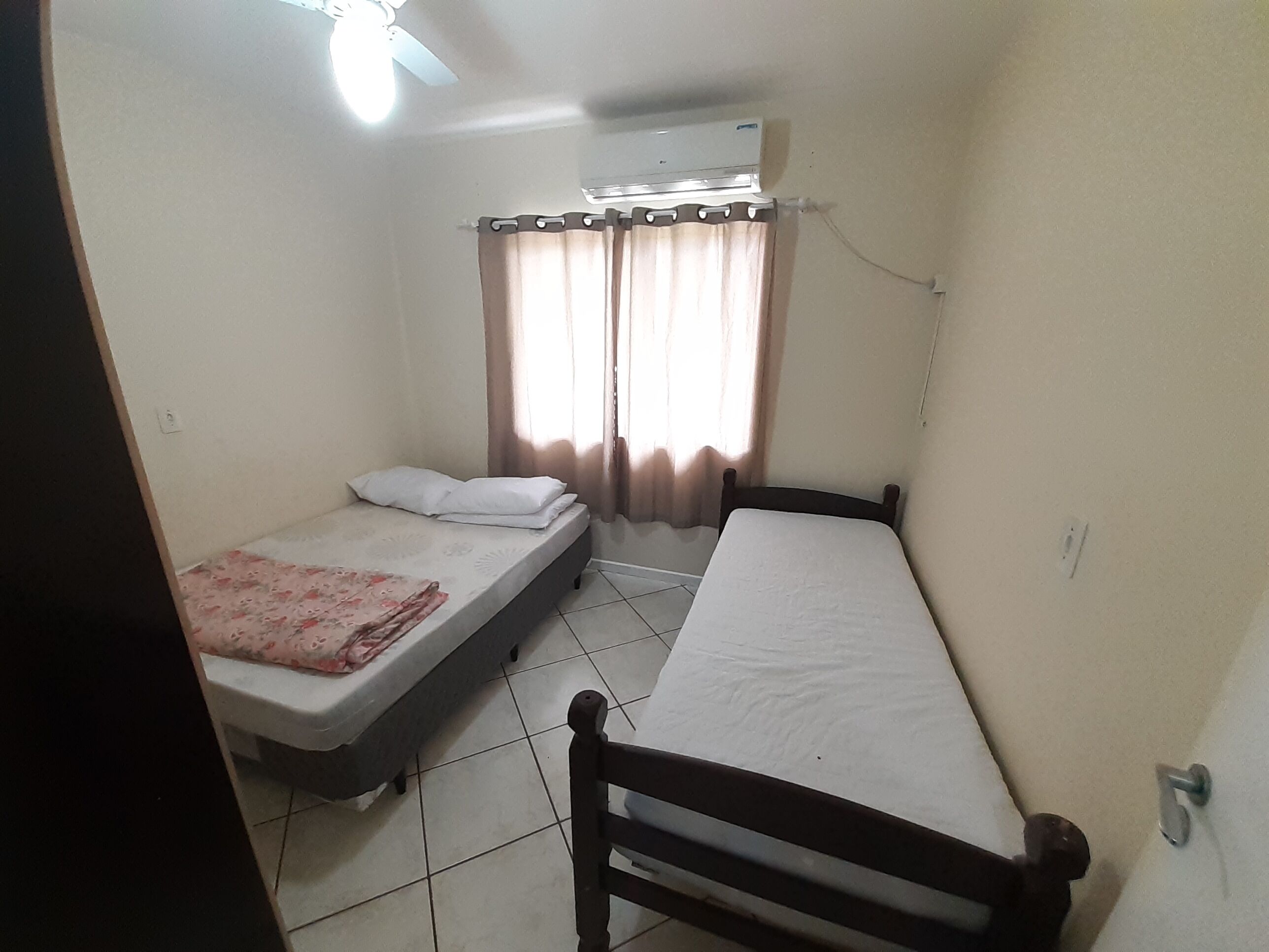 A small, clean room with two single beds, a ceiling fan, and an air conditioning unit.