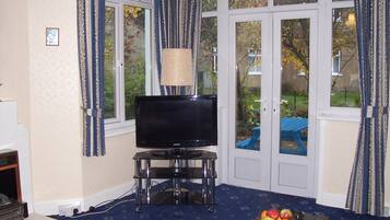 A living room with a television on a stand, a lamp, and a table with fruit.