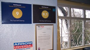 Un mur où sont affichés divers prix et mentions, notamment une note de 9,1 sur Booking.com, une note de 9 attribuée par les Traveller Review Awards 2020, et une mention concernant Arrow Universal Private Hire.