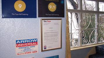 A wall with various awards and notices, including a 9.1 rating from Booking.com, a 9 rating from Traveller Review Awards 2020, and a notice for Arrow Universal Private Hire.