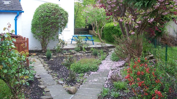 Un jardin avec un chemin de pierres, une clôture en bois et un banc bleu.