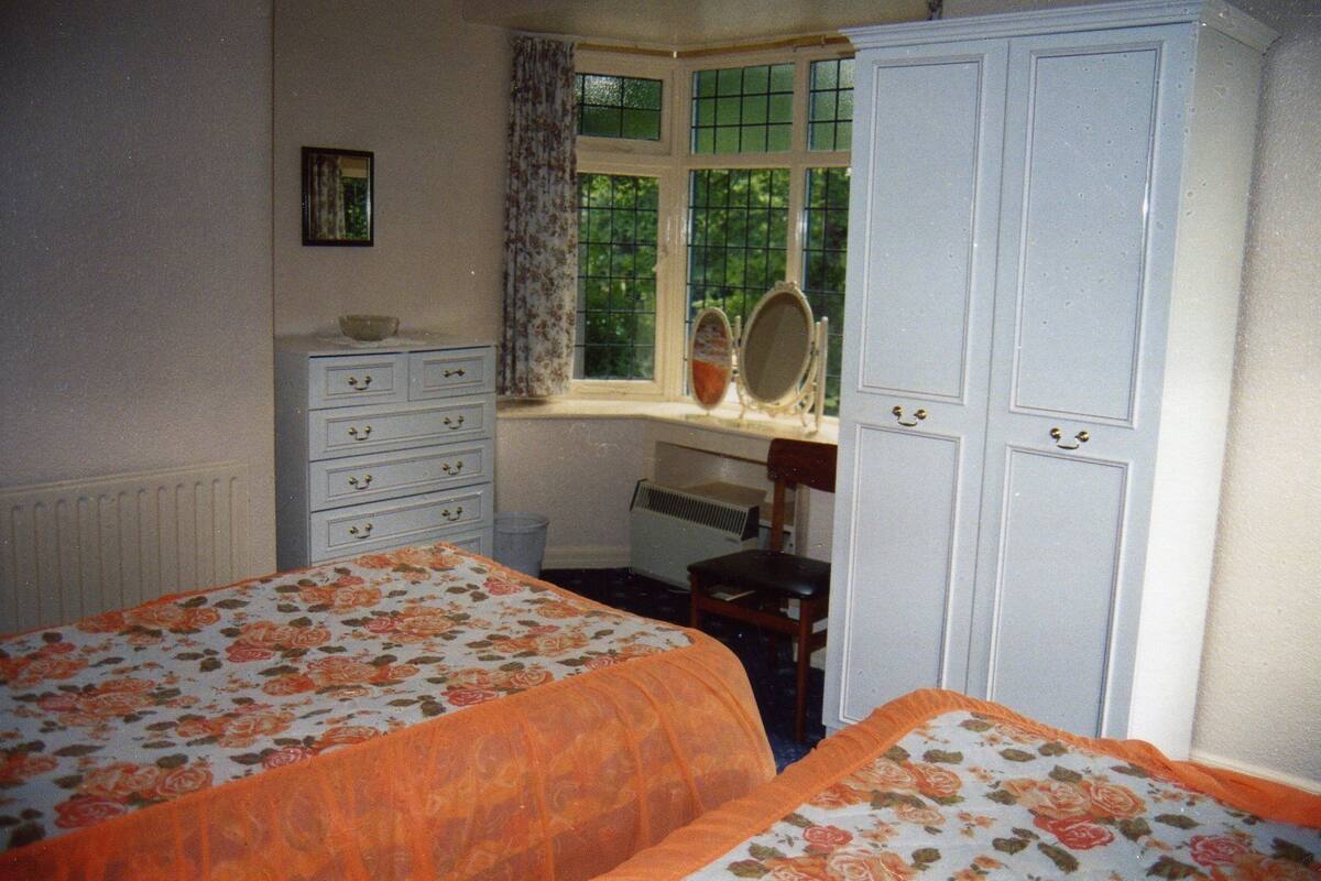 A bedroom with two beds, a dresser, a window with curtains, a mirror, and a radiator.