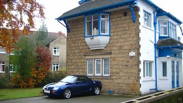 A two-story house with a stone facade and blue trim, a parked car in front, and a number '153' on the wall.