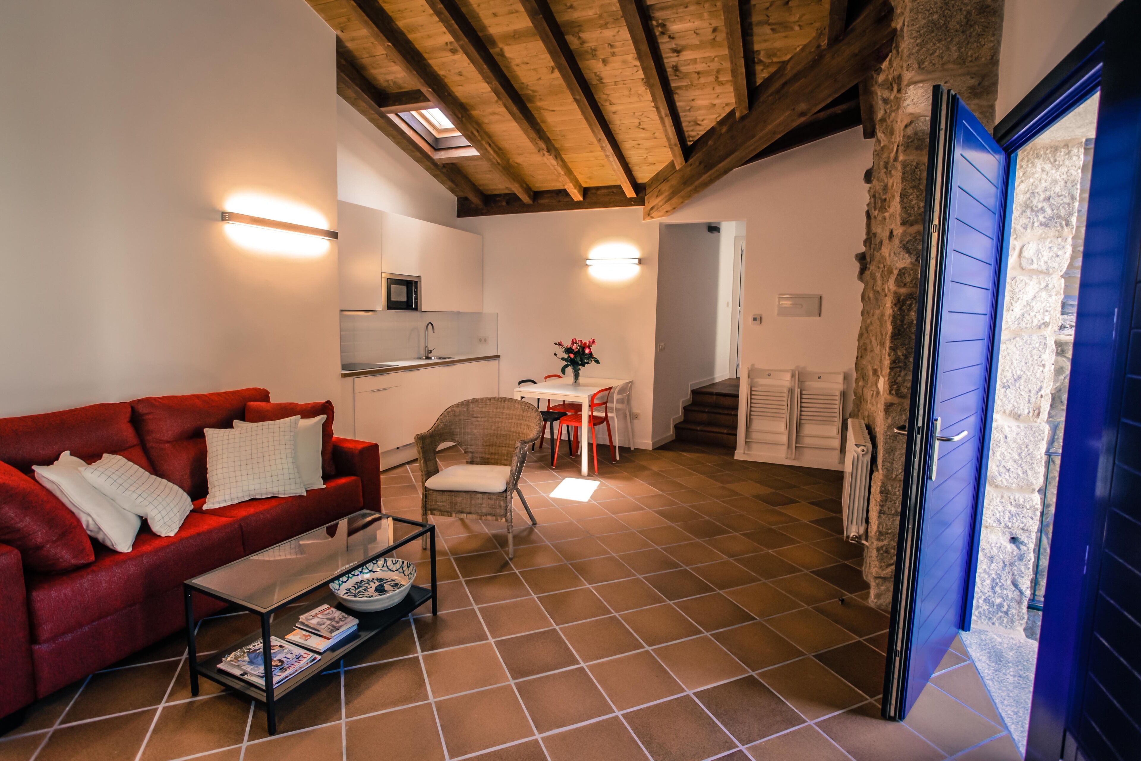 Un salon chaleureux avec un canapé rouge, une table basse en verre et un coin repas comprenant une table blanche et des chaises rouges.
