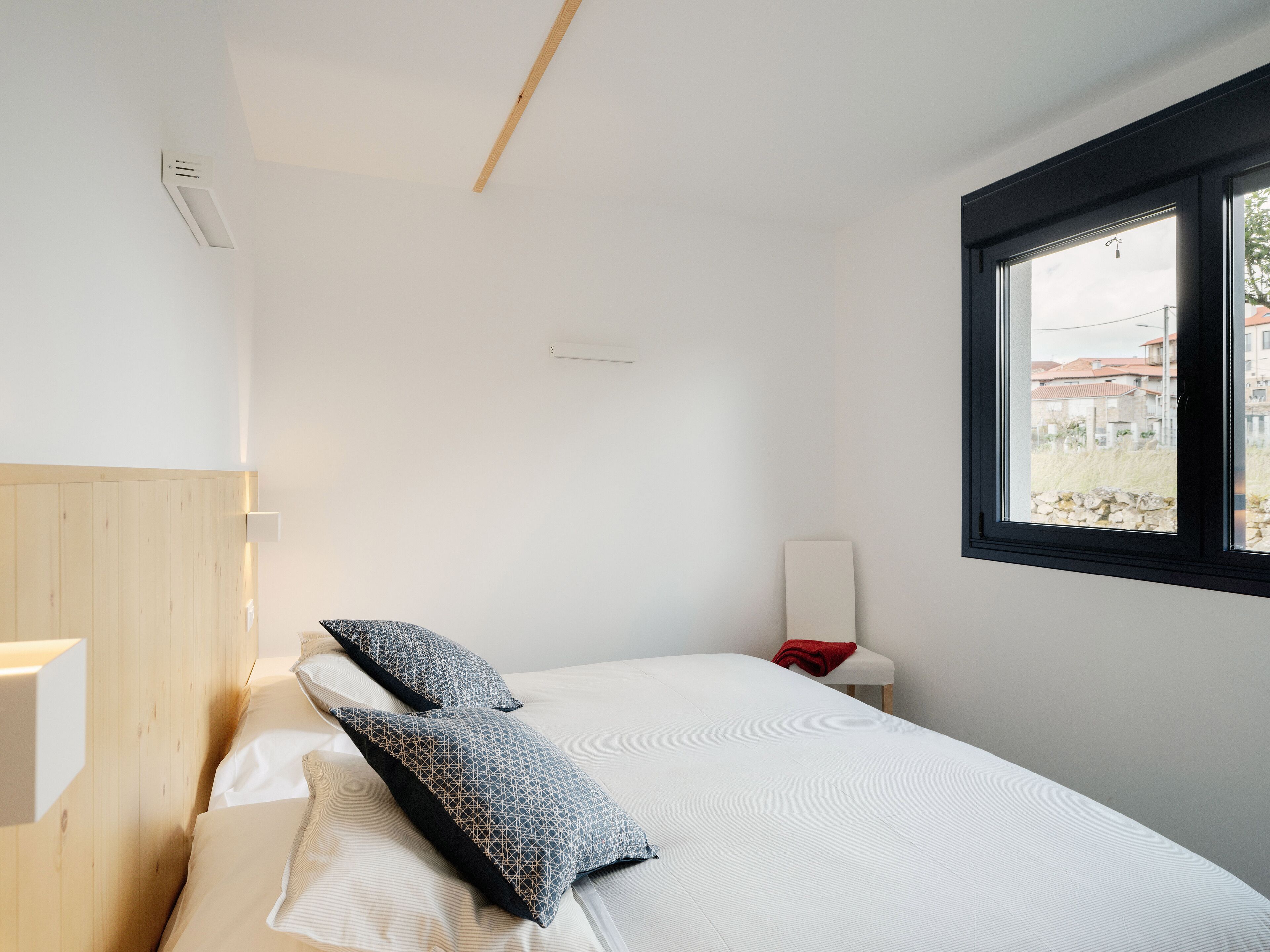 A minimalist bedroom with a bed, pillows, a nightstand, and a window with a view of buildings.