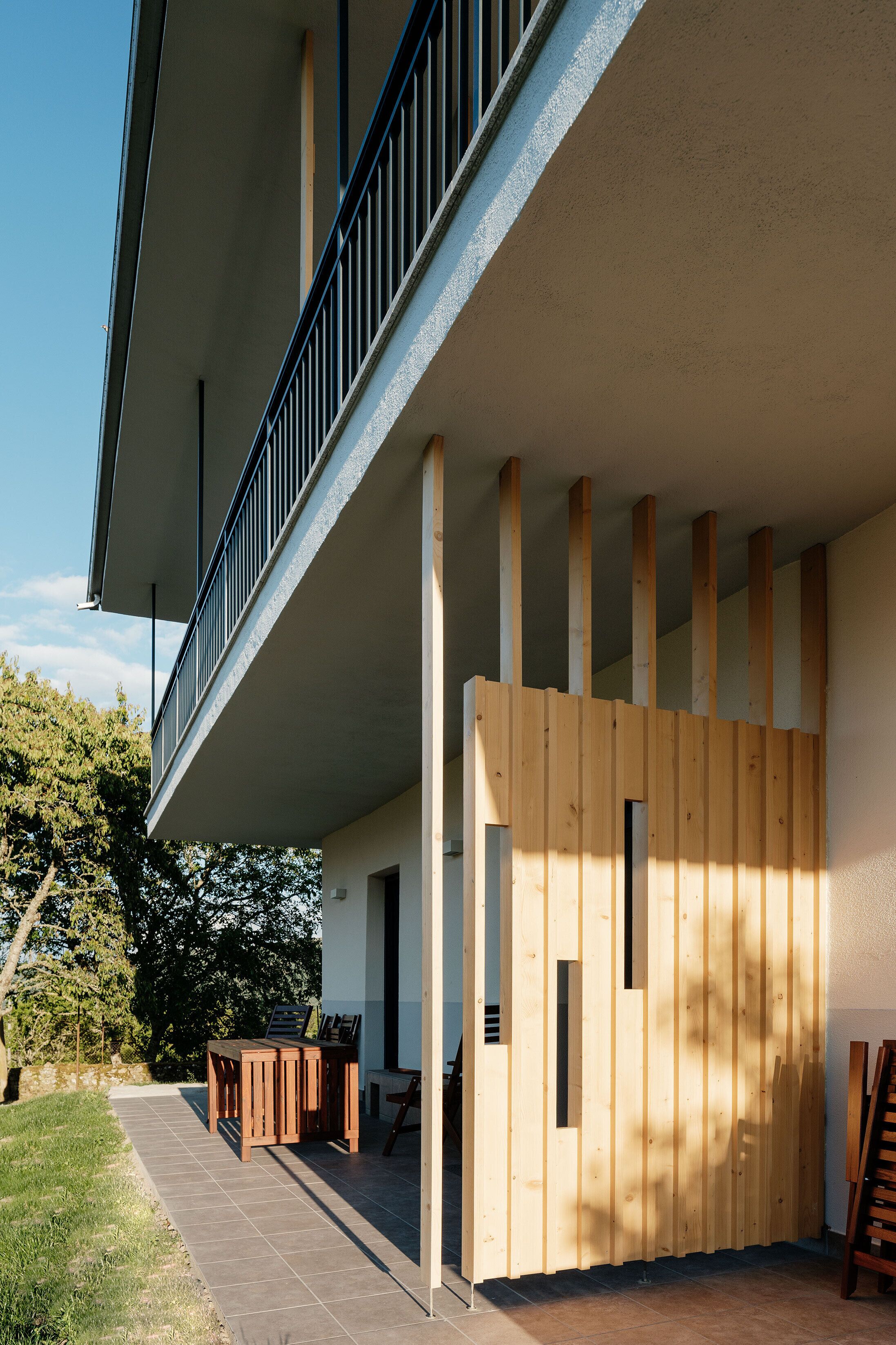 A modern building with a balcony, wooden paneling, and outdoor seating.