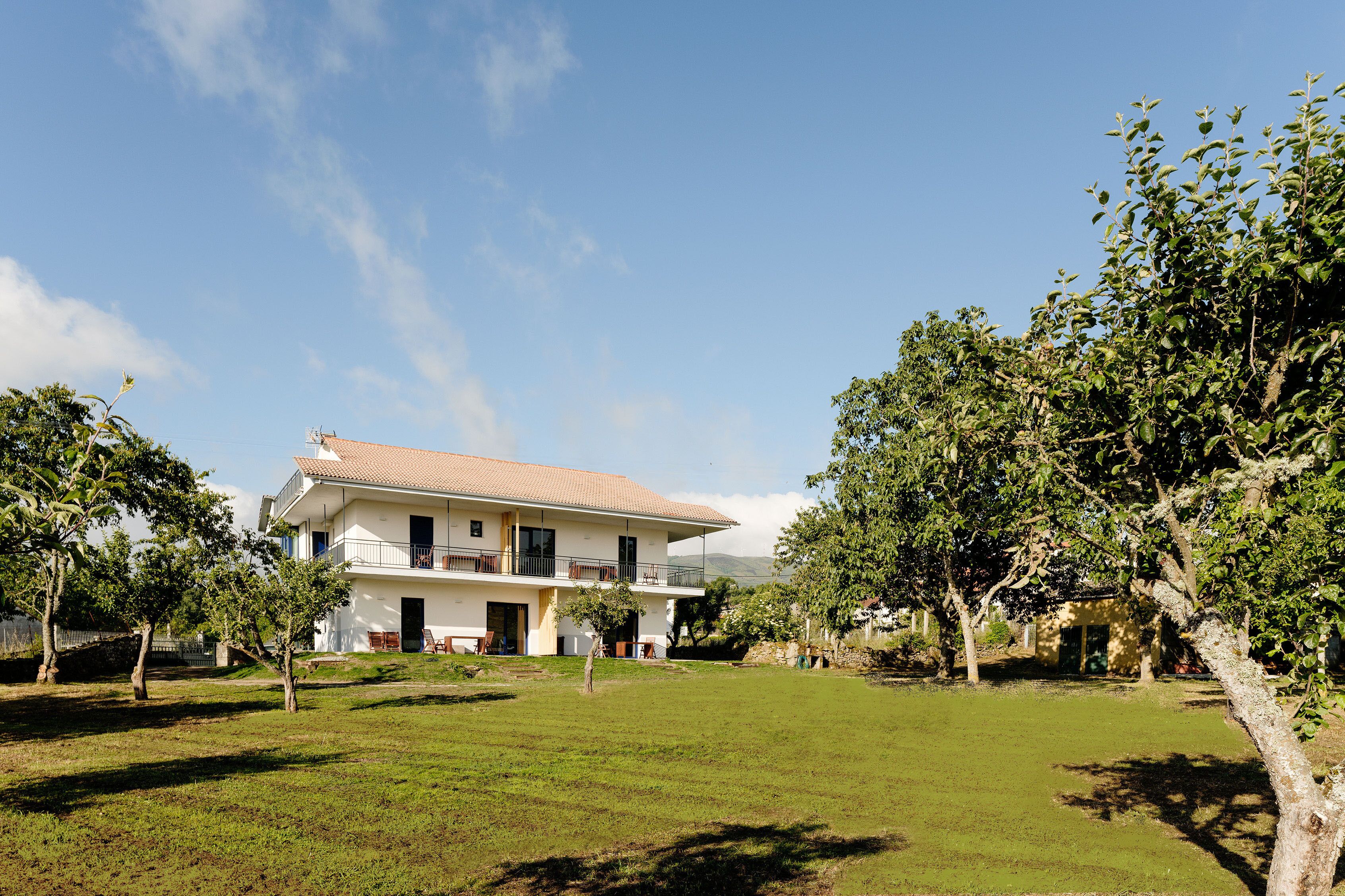 A two-story house with a balcony, surrounded by a grassy yard and trees.